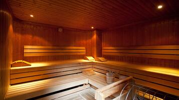 Una sauna con bancos de madera, una mesita y un estante metálico.