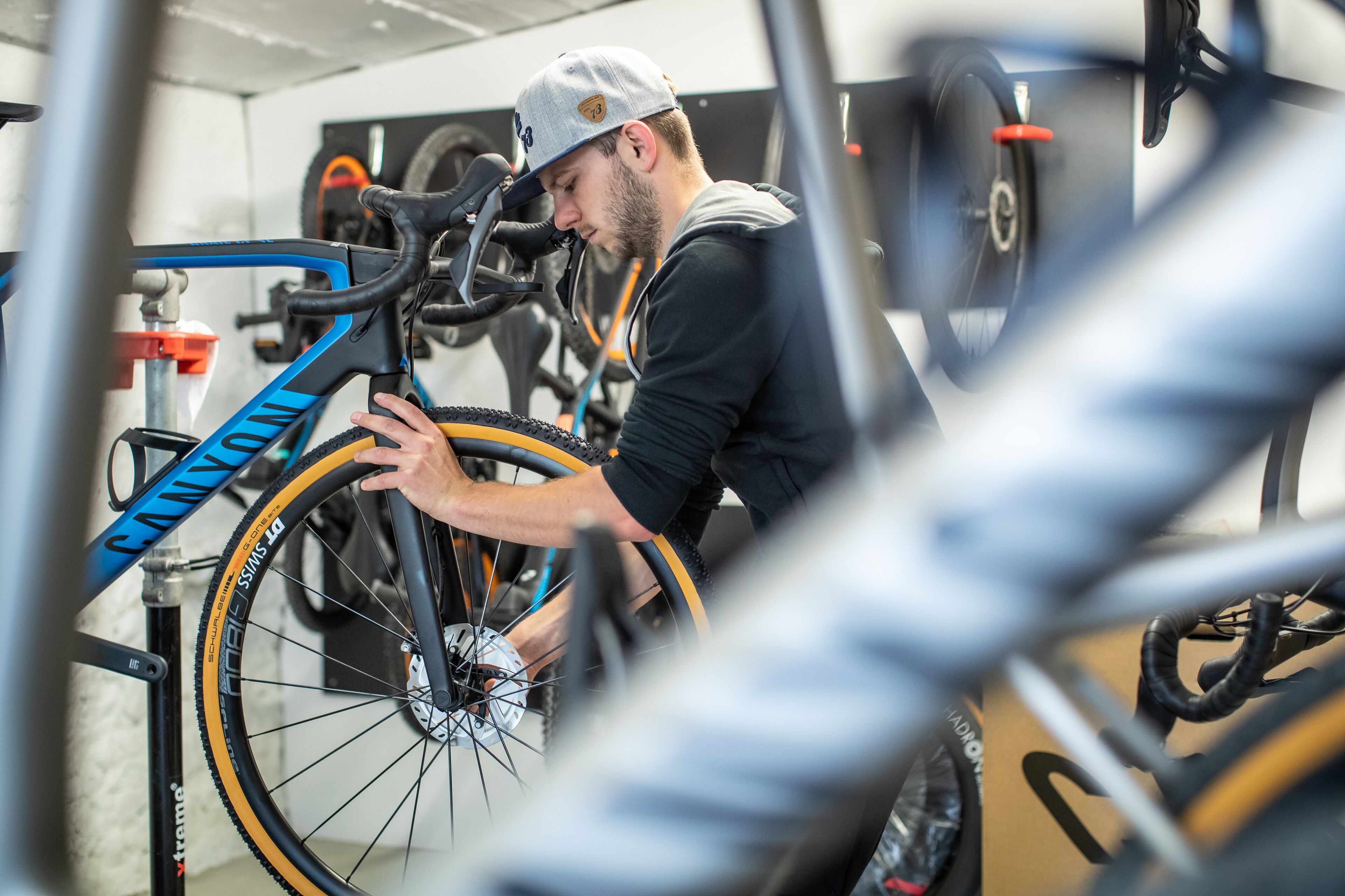 A person adjusting a bicycle in a well-lit indoor space with multiple bicycles and a visible ceiling structure.