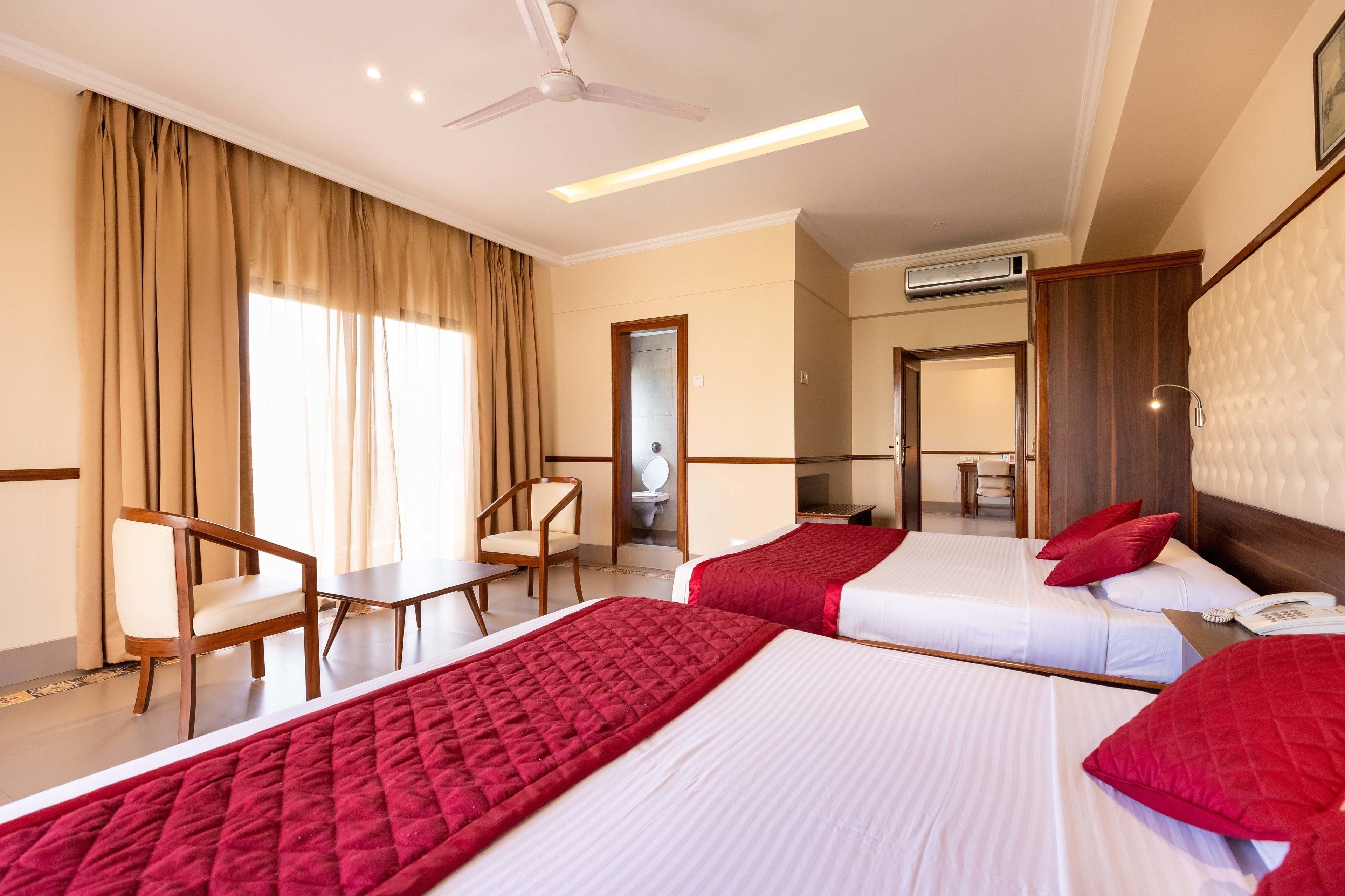 A hotel room with two beds, a desk, a chair, and a bathroom visible through an open door.