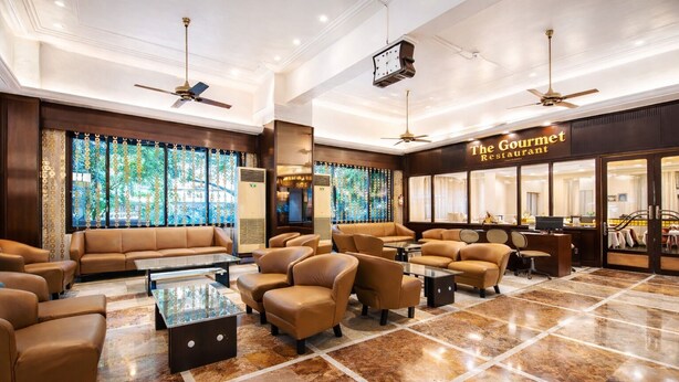 Een hotel lobby met een zithoek, een receptiebalie en een bord met de tekst 'The Gourmet Restaurant'.