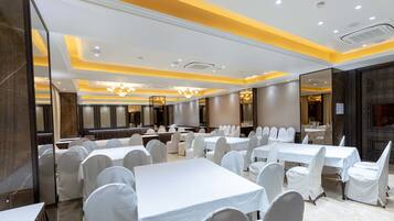 Un salón de banquetes con varias mesas y sillas, iluminación empotrada y suelo de mármol.