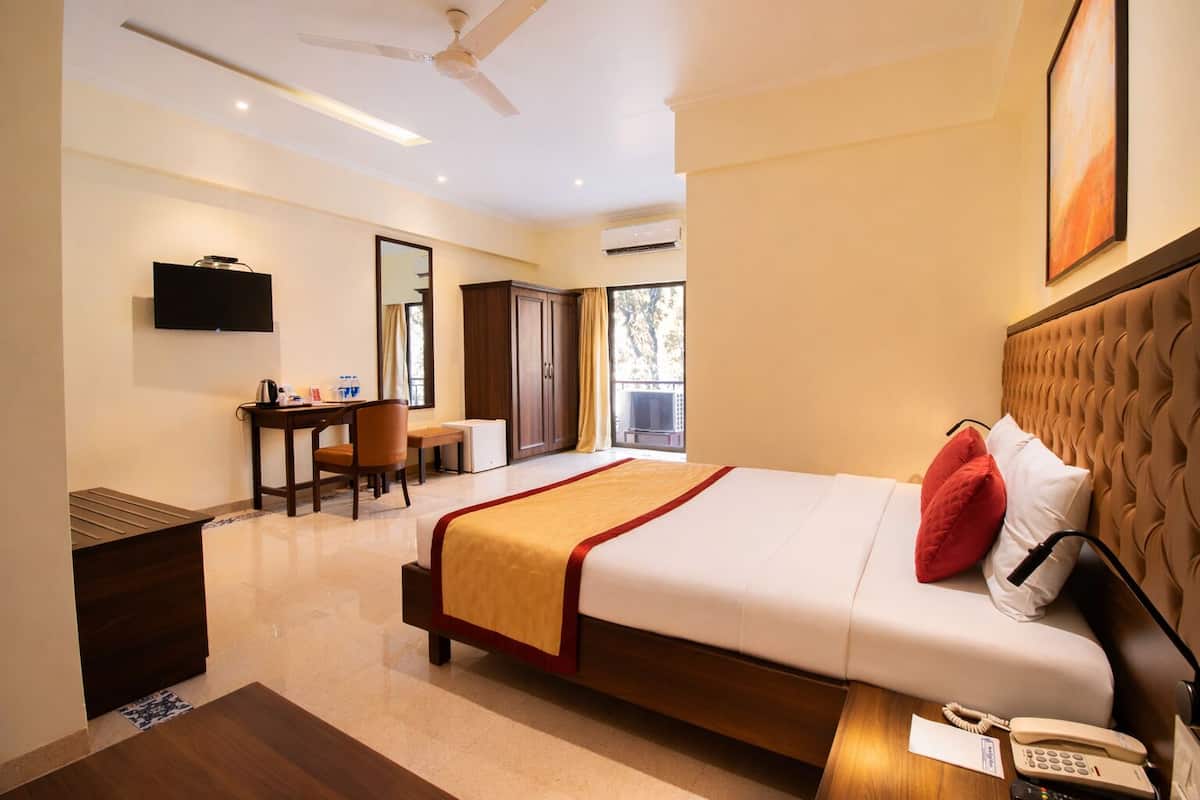 A hotel room with a bed, bedside table, a desk with a chair, a wardrobe, a television, and a ceiling fan.