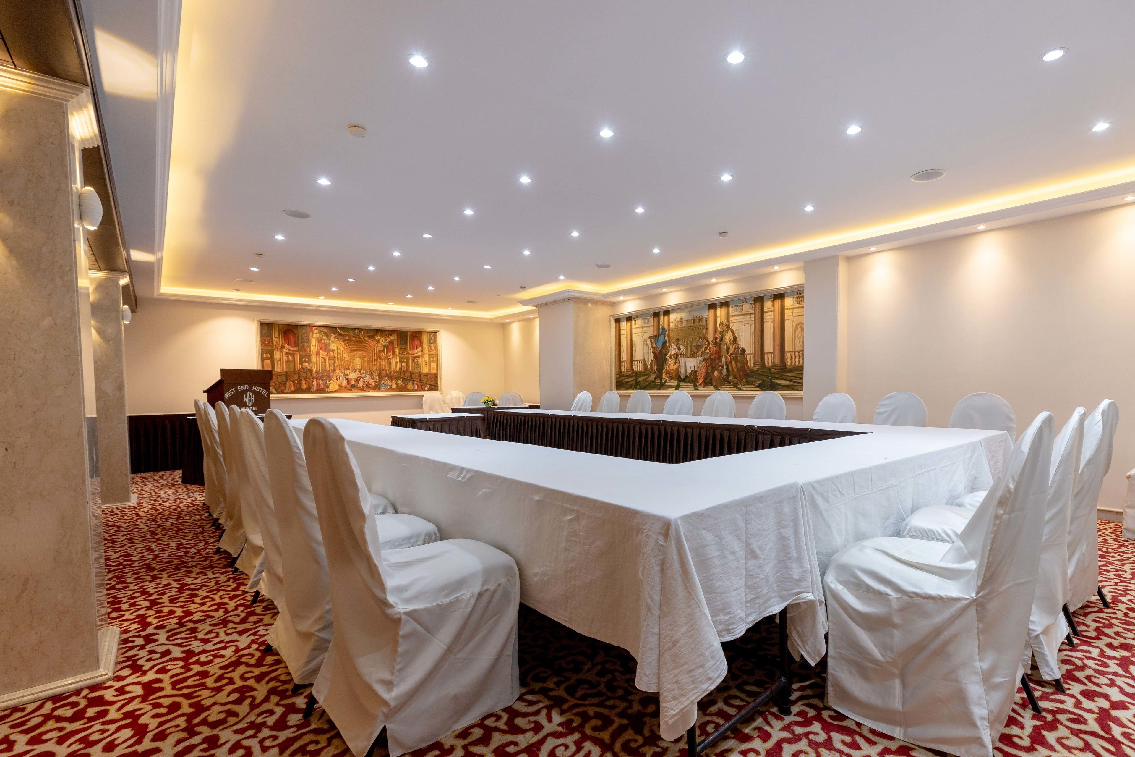 A conference room with a long table, white chairs, and a red patterned carpet.
