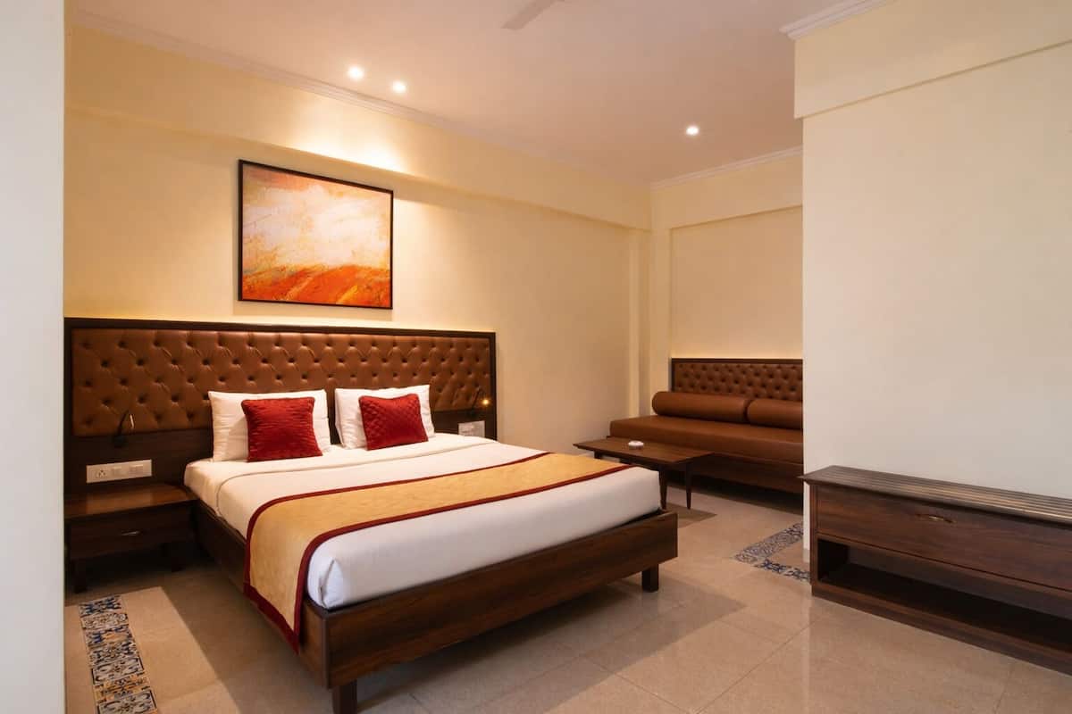 A hotel room with a large bed, a sofa, a TV, and a painting on the wall.