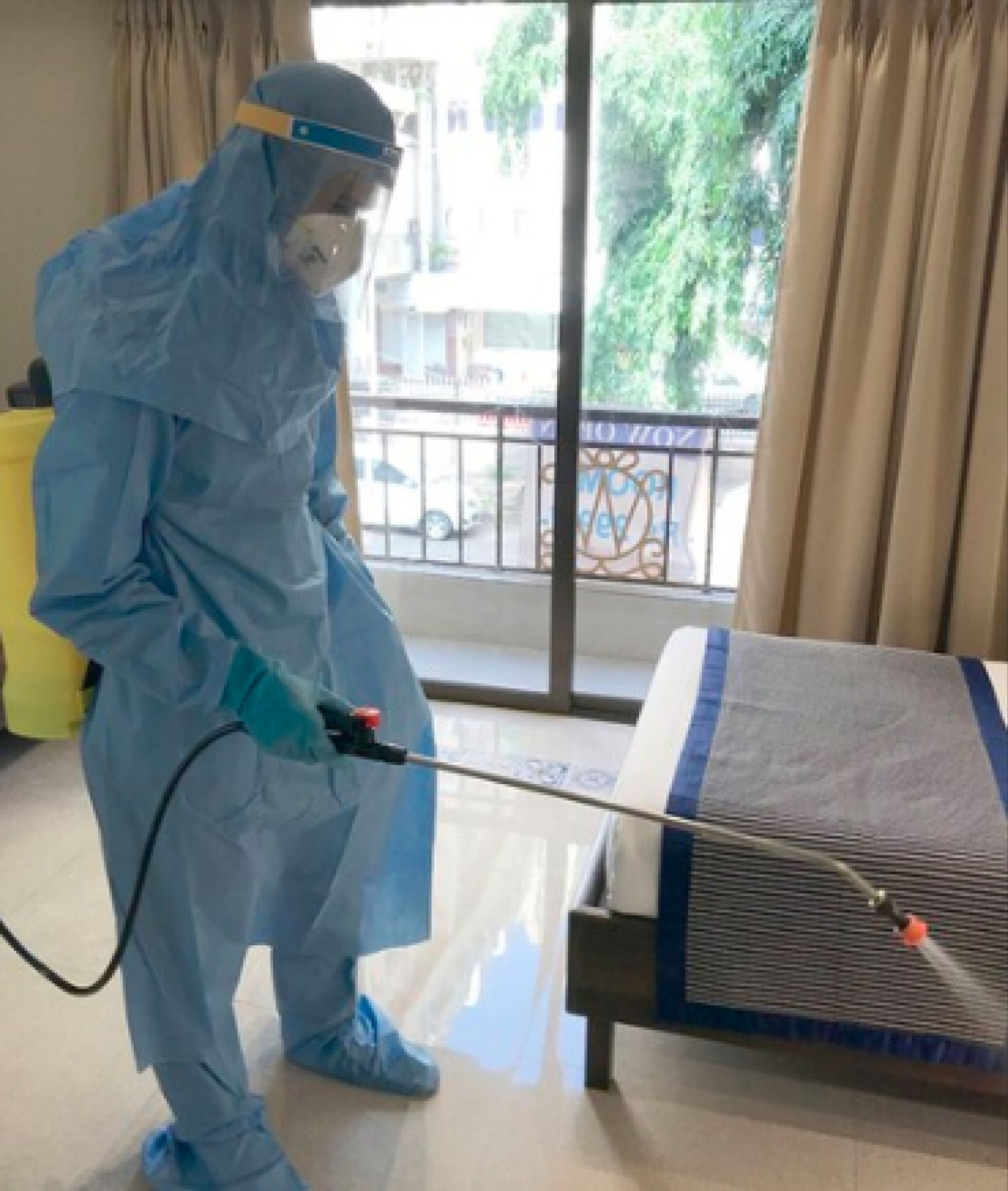 Une personne, vêtue d'une combinaison de protection, nettoie un lit à l'aide d'un vaporisateur.
