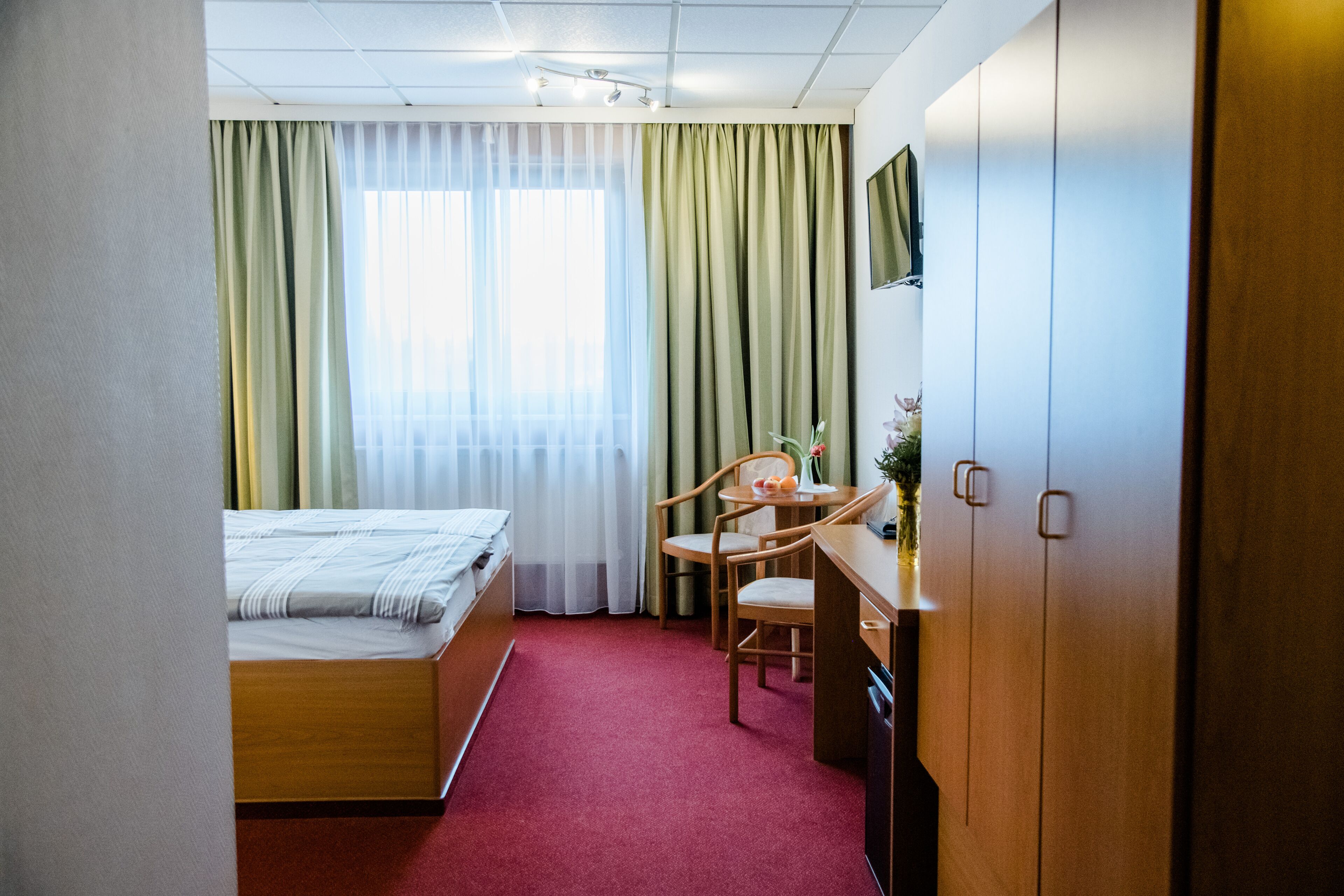 Une chambre d’hôtel avec un lit, un bureau et une chaise, un téléviseur fixé au mur et des rideaux à la fenêtre.