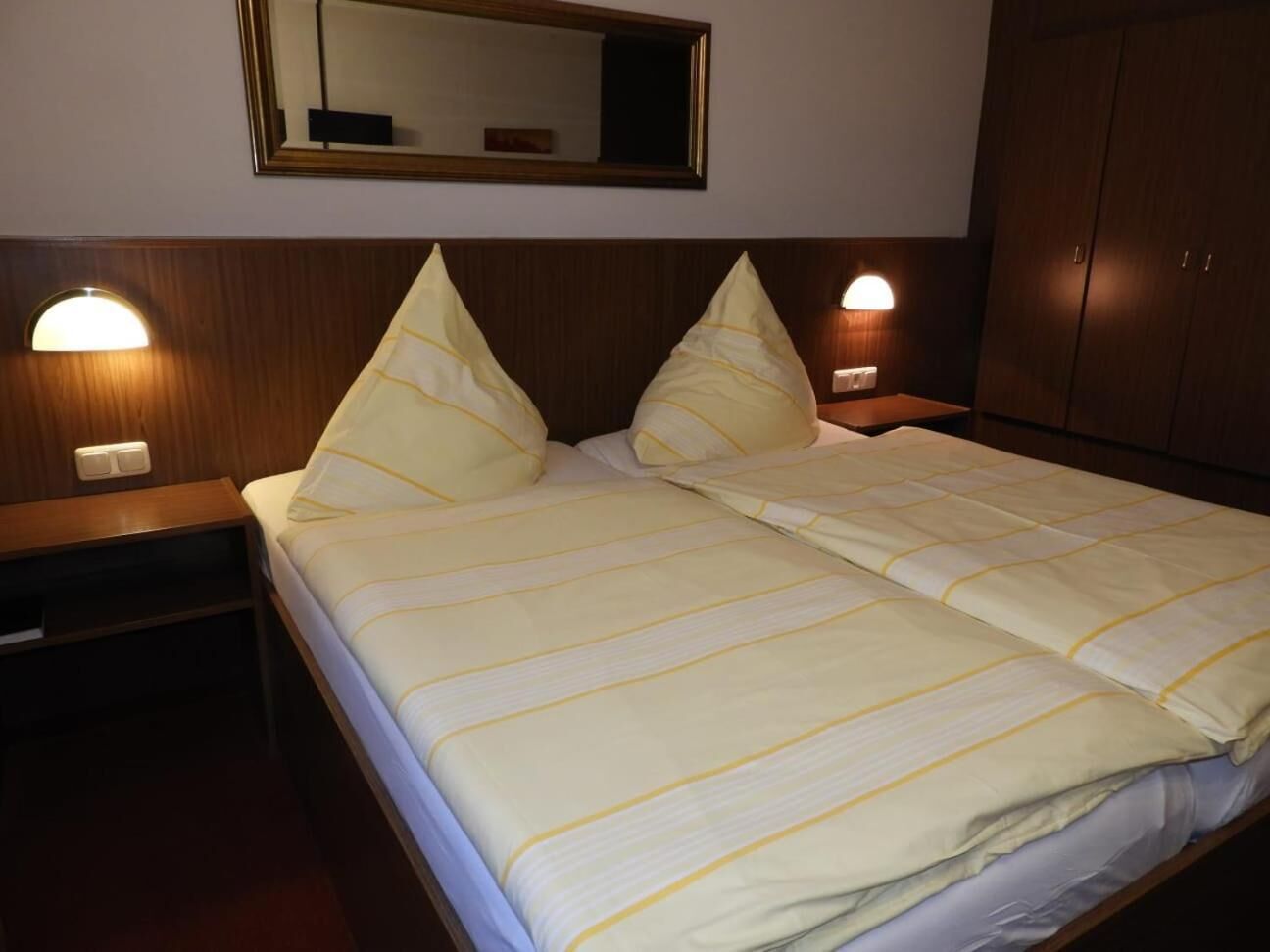 A hotel room with a bed, two bedside lamps, a mirror, and a wardrobe.