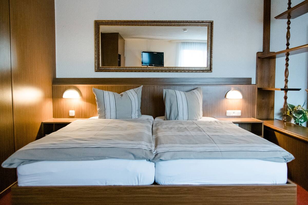 Uma cama de casal com cabeceira de madeira, duas luminárias laterais e um espelho grande sobre a cama.
