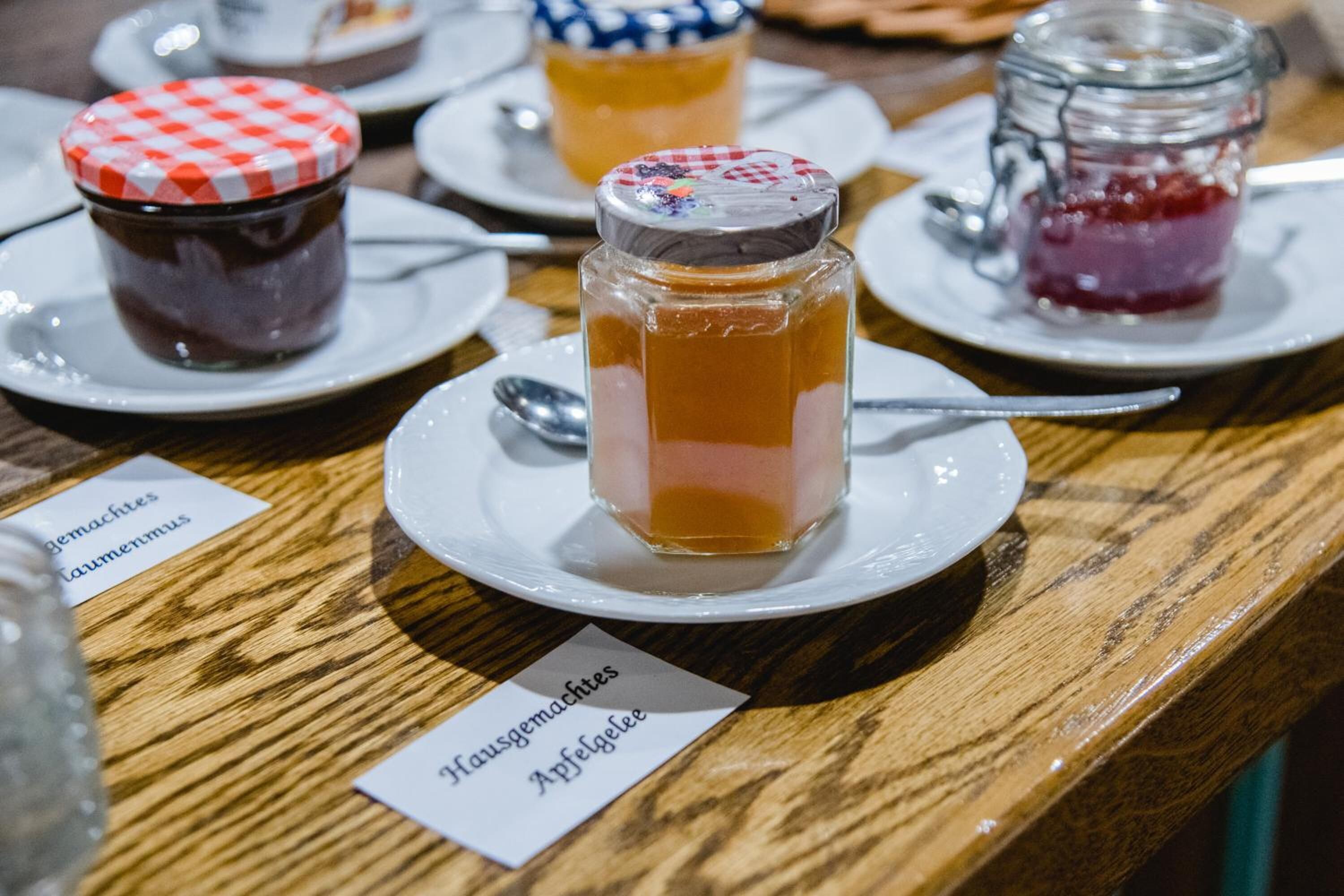 Uma mesa de madeira com vários potes de geleia e compotas, cada um identificado com seu nome.