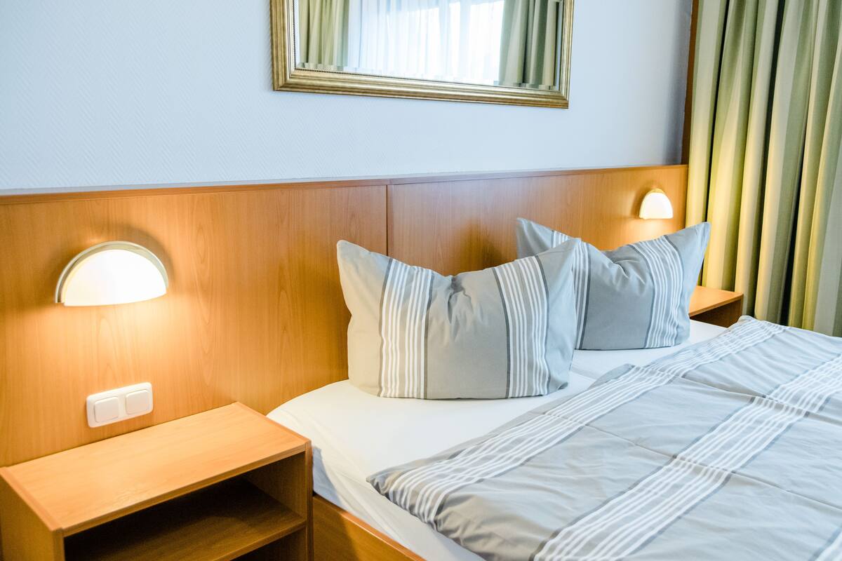 Quarto de hotel com cabeceira de madeira, cama com roupa de cama listrada, duas luminárias de cabeceira e uma mesa de cabeceira.