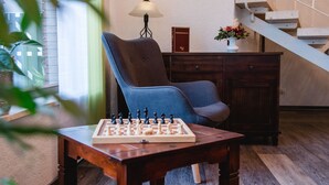 A chessboard on a wooden table, a blue armchair, a lamp, a book, and a vase with flowers. - Hotel Müller (Genthin)