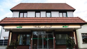 A hotel with a tiled roof, a glass entrance, and two potted plants in front. - Hotel Müller (Genthin)