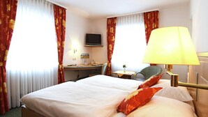 A hotel room with a bed, a desk, a chair, a TV, and a lamp.