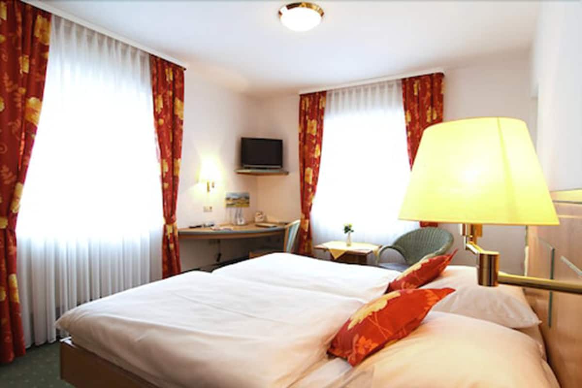A hotel room with a bed, a desk, a chair, a TV, and a lamp.