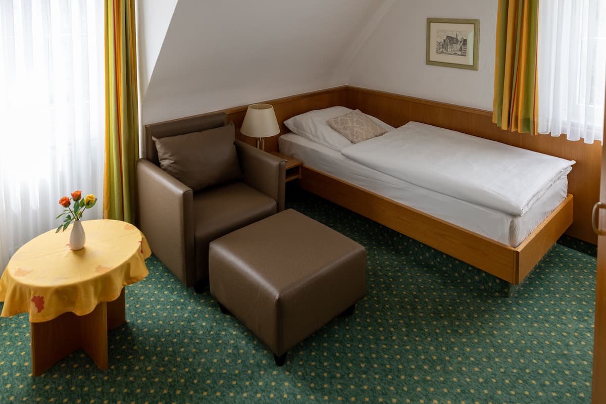 A compact hotel room with a bed, a sofa, a small table with a vase, and a lamp.