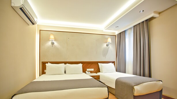 A hotel room with a large bed, a smaller bed, a nightstand, an air conditioning unit, and a window with curtains. -  Sogut Hotel Old City (Istanbul)