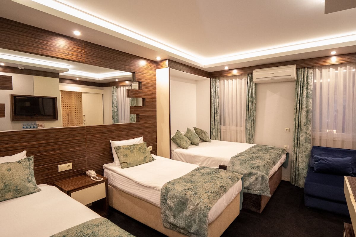 A hotel room with two beds, a desk, a TV, and an air conditioning unit.