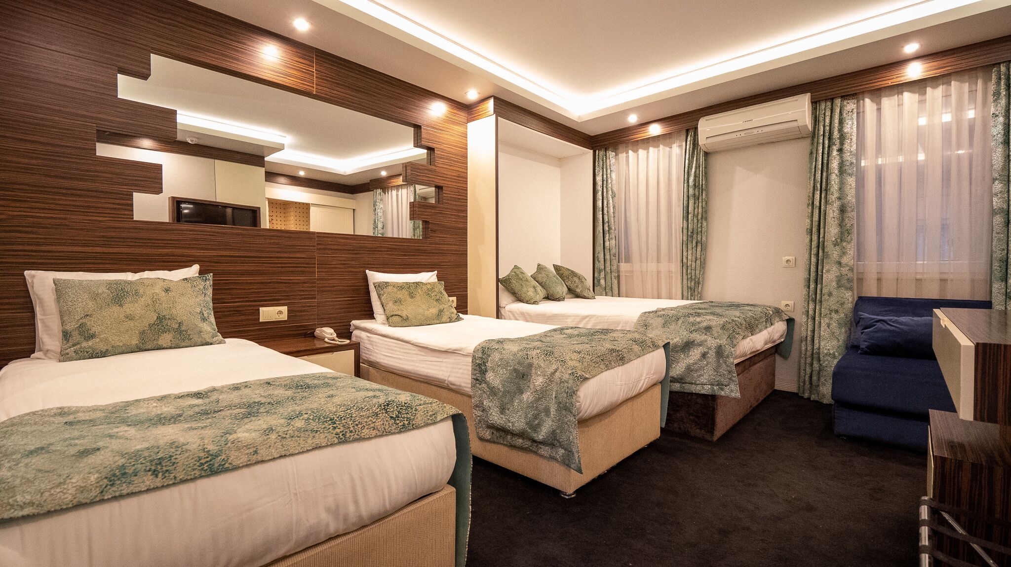 A hotel room with two beds, a sofa, a mirror, and a ceiling light.