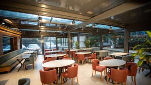 A modern cafe with round tables and cushioned seating, large windows, and a view of parked cars outside. -  Sogut Hotel Old City (Istanbul)