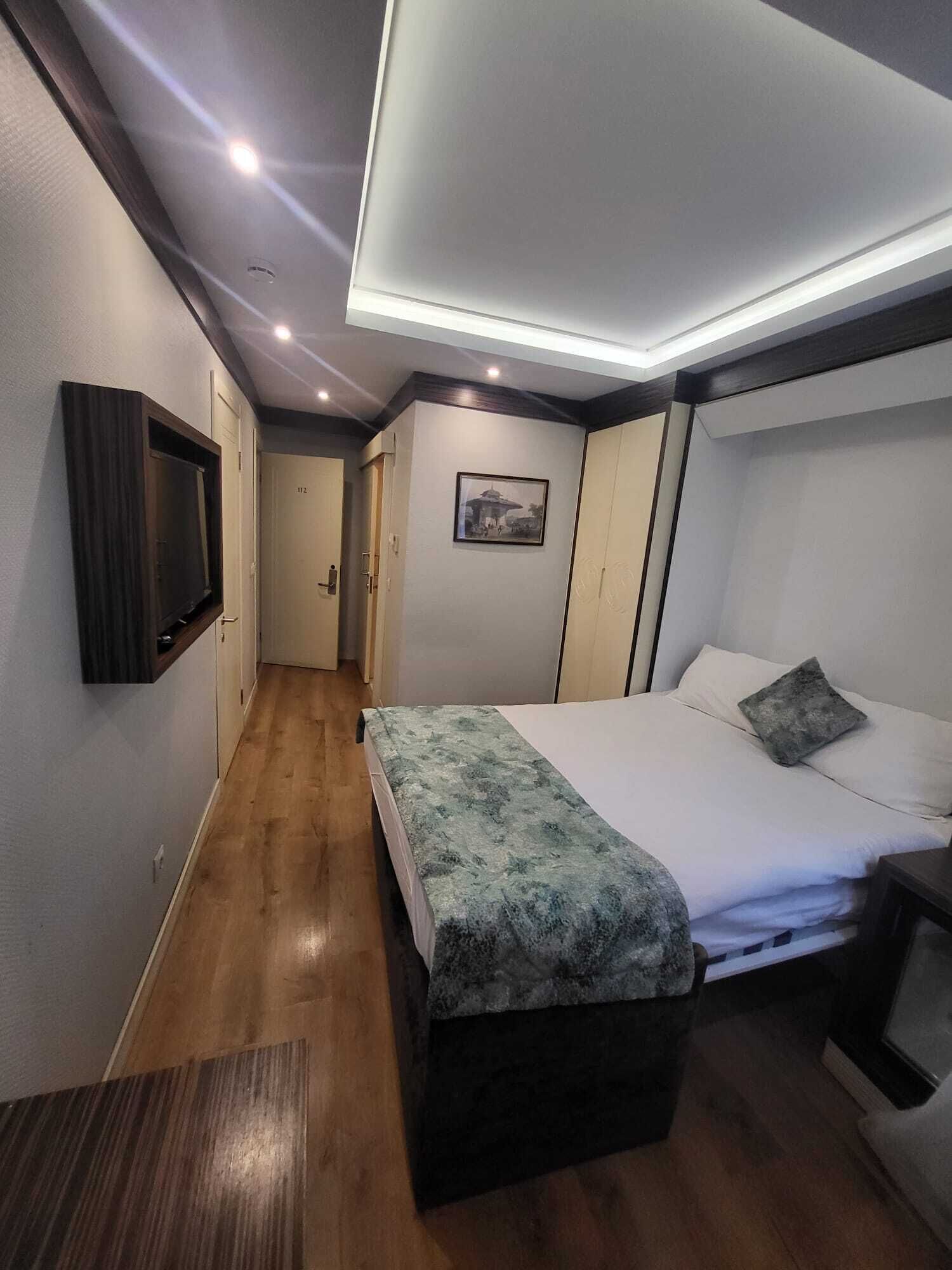 A hotel room with a bed, bedside table, and a television mounted on the wall.