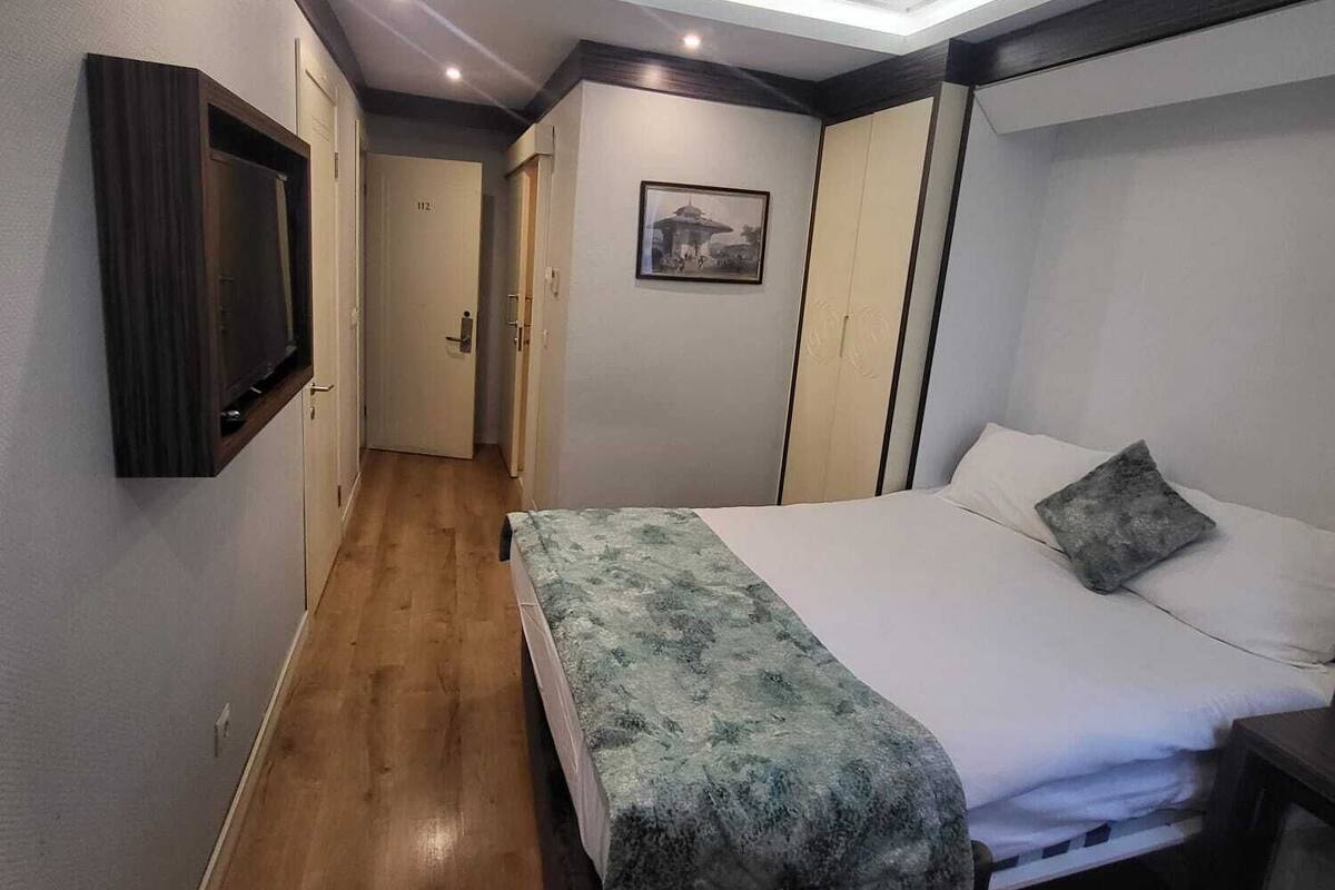 A hotel room with a bed, bedside table, and a television mounted on the wall.