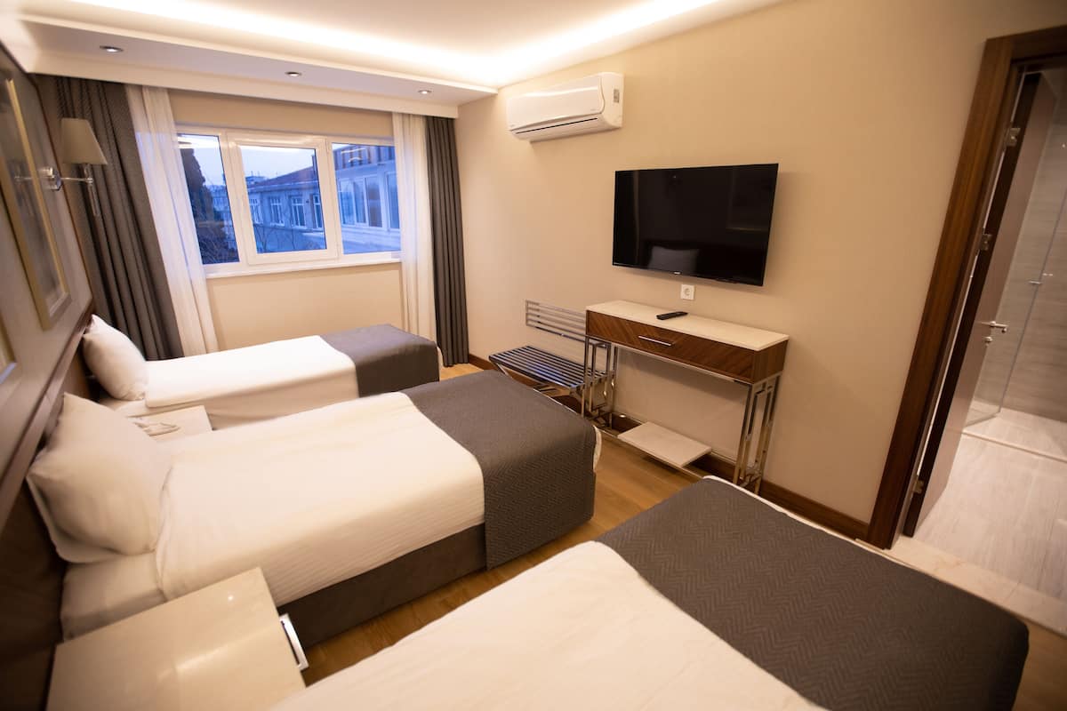 A hotel room with two beds, a TV, a desk, and a window with a view.
