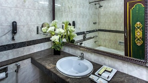 A bathroom with a marble sink, a mirror, a shower, and a decorative plant. - Hotel Sunstar Residency (New Delhi)