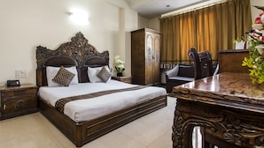 A hotel room with a large bed, a wooden nightstand, a wardrobe, a dining table, and a chair. - Hotel Sunstar Residency (New Delhi)