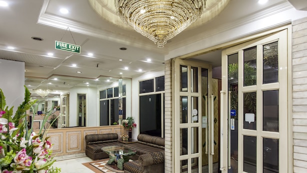 A lobby with a fire exit sign, a chandelier, a sofa, a coffee table, and a mirror reflecting the room. - Hotel Sunstar Residency (New Delhi)