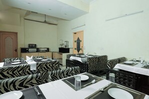 A dining area with zebra-patterned upholstery, a central serving station, and a door with decorative glass panels. - Hotel Sunstar Residency (New Delhi)