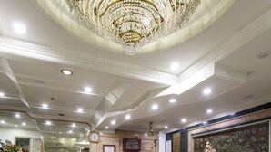 A hotel reception area with a marble counter, a large chandelier, and a clock on the wall. - Hotel Sunstar Residency (New Delhi)