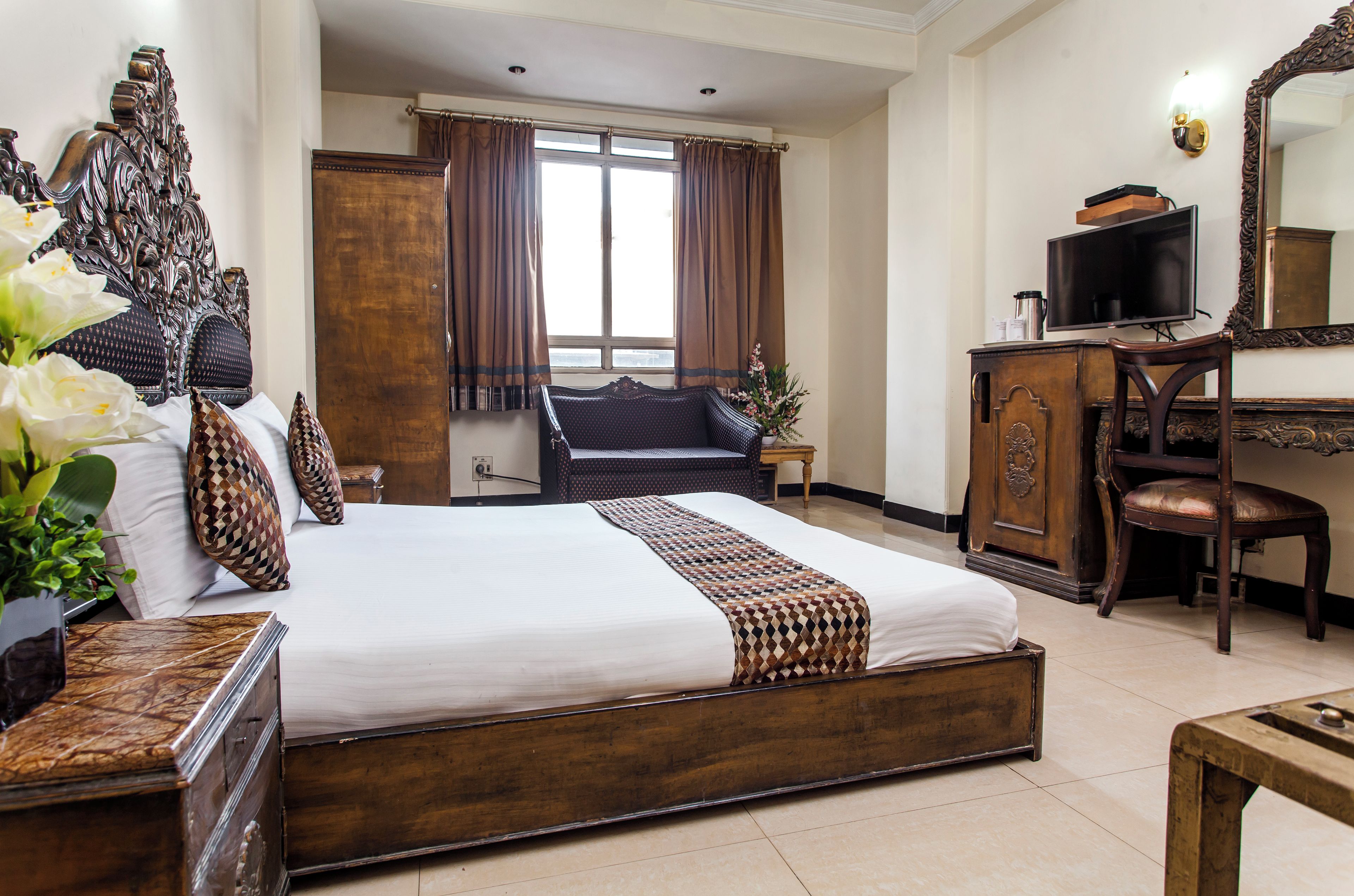 A hotel room with a large bed, a wooden dresser, a television, and a desk.
