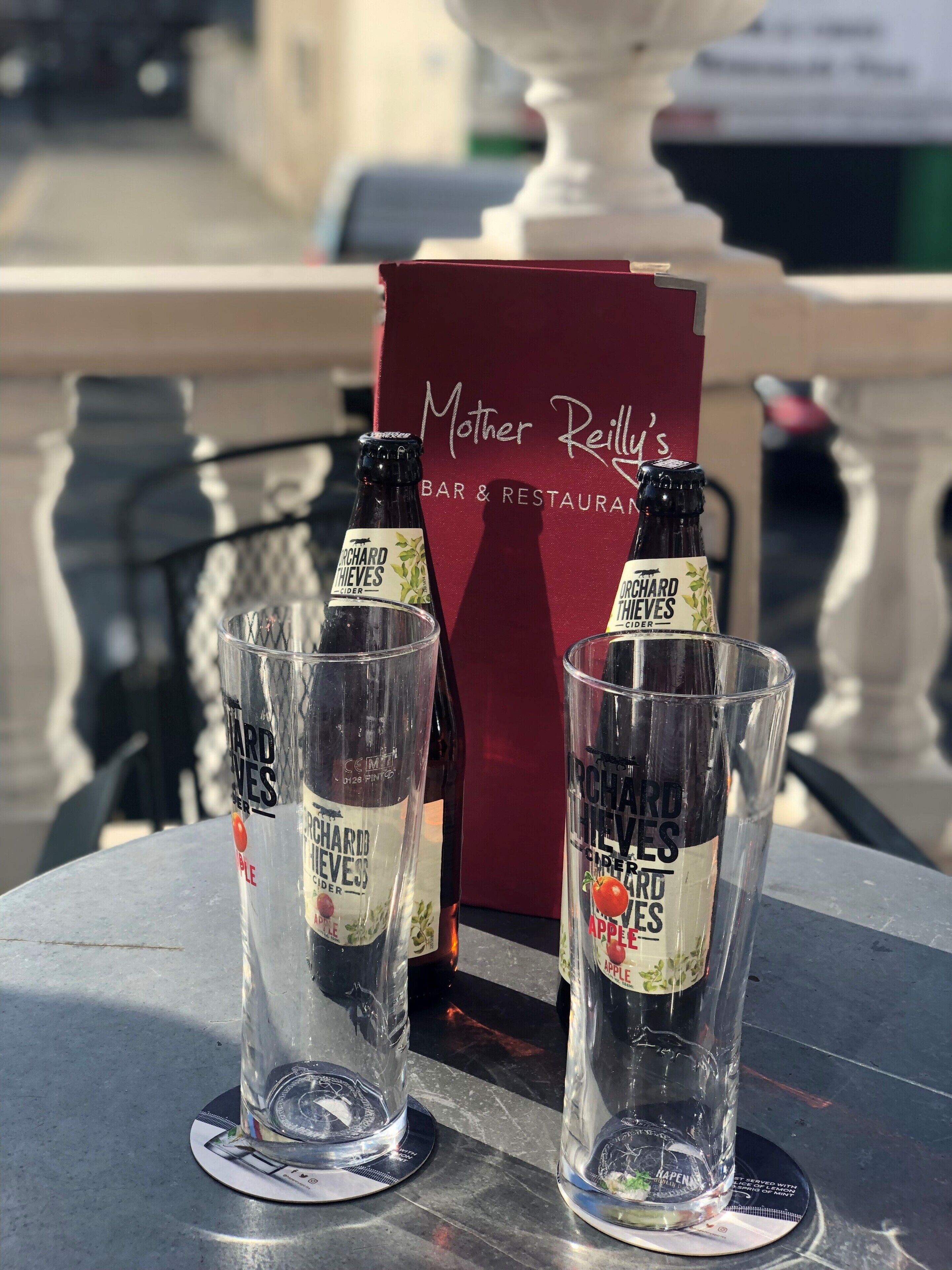 Dos botellas de sidra de Richard Reilly y dos vasos sobre una mesa, con un menú rojo al fondo.