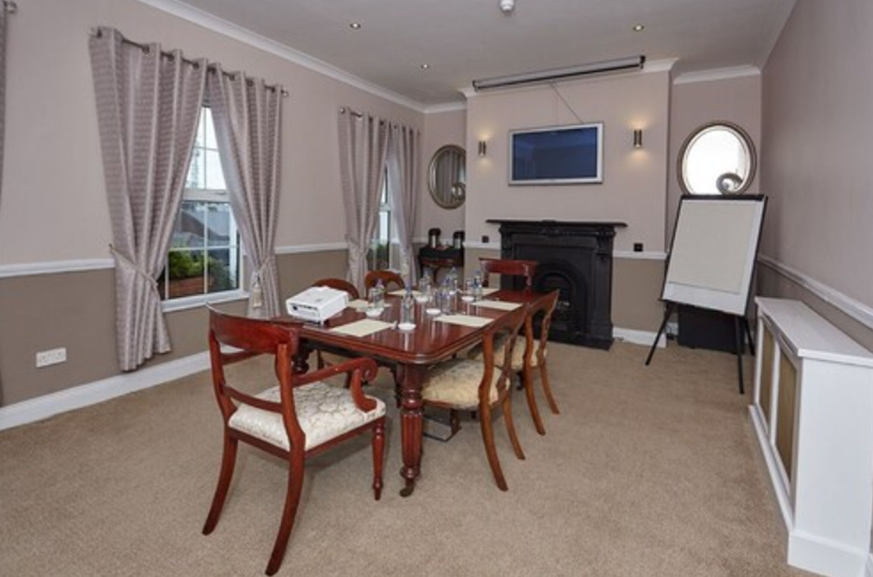 A conference room with a wooden table, chairs, a fireplace, a whiteboard, and a large window with curtains.