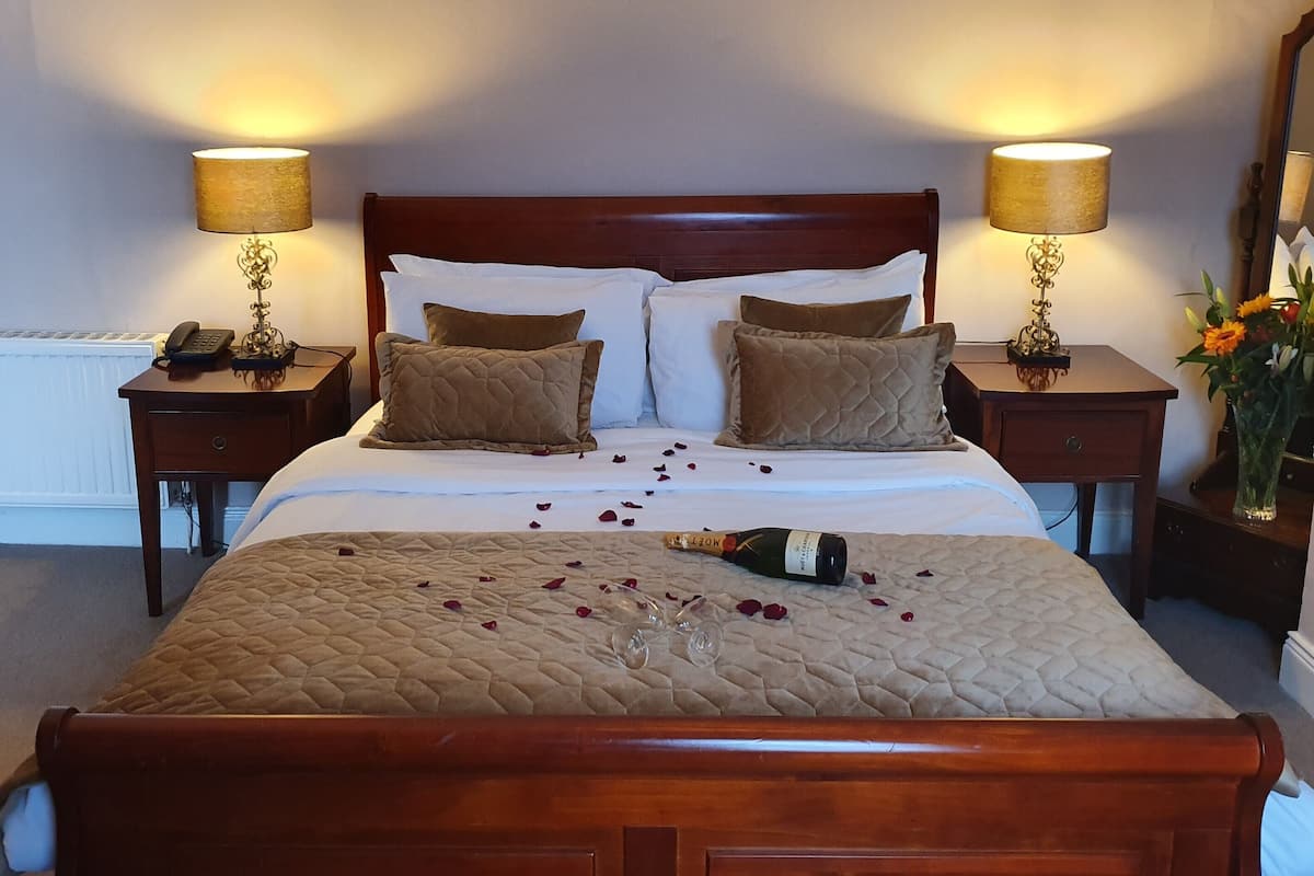 Ein ordentlich bezogenes Bett mit einer gesteppten Decke, zwei Nachttische mit Lampen, ein Spiegel und eine Vase mit Blumen.
