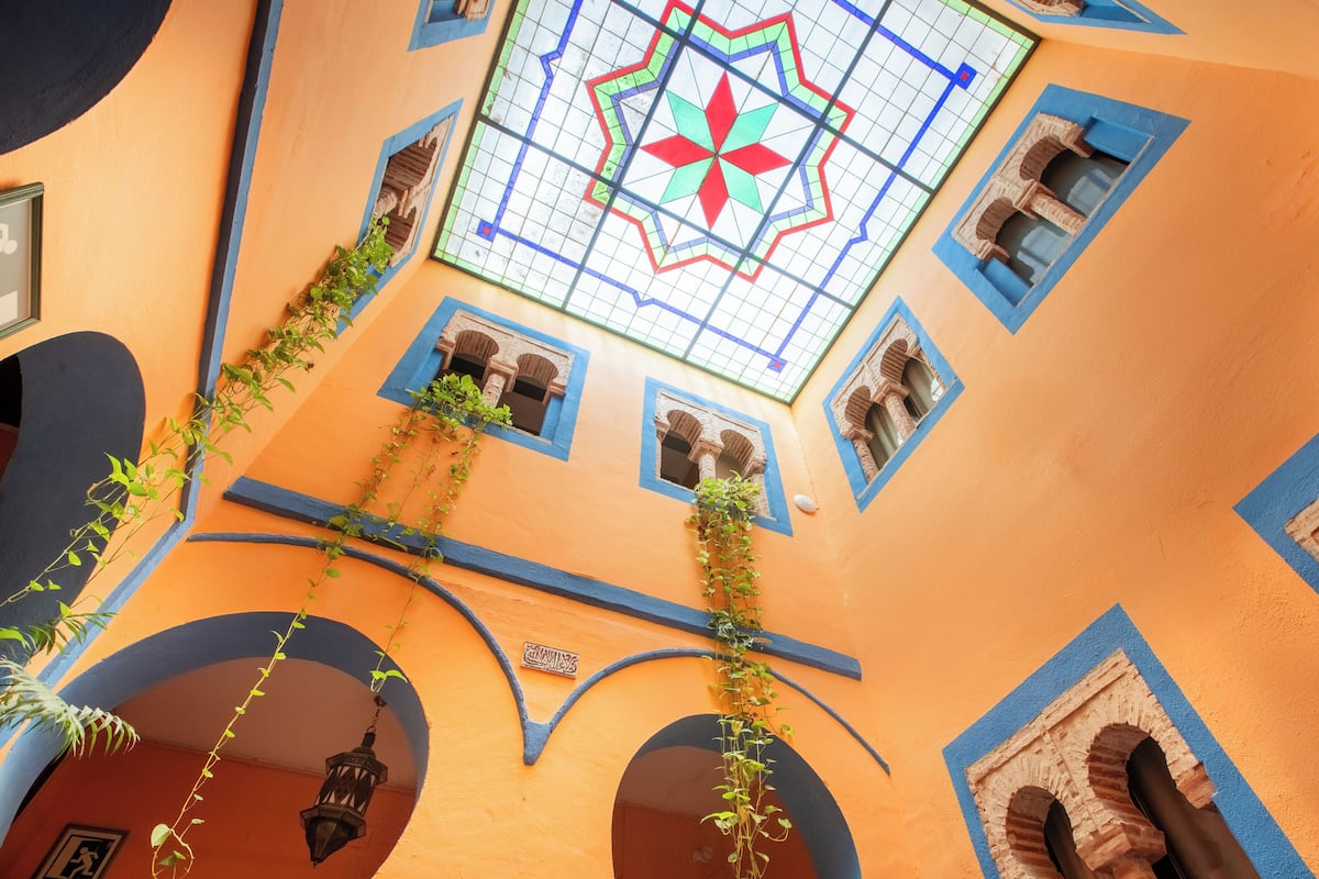 Una habitación con piso de baldosas, una ventana con diseño geométrico y una planta colgante.