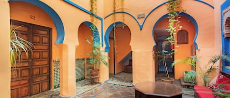 A courtyard with arches, a wooden door, tiled flooring, and potted plants.