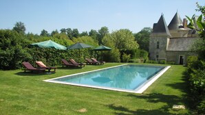 Piscina rectangular con césped alrededor, varias sillas de descanso y sombrillas.