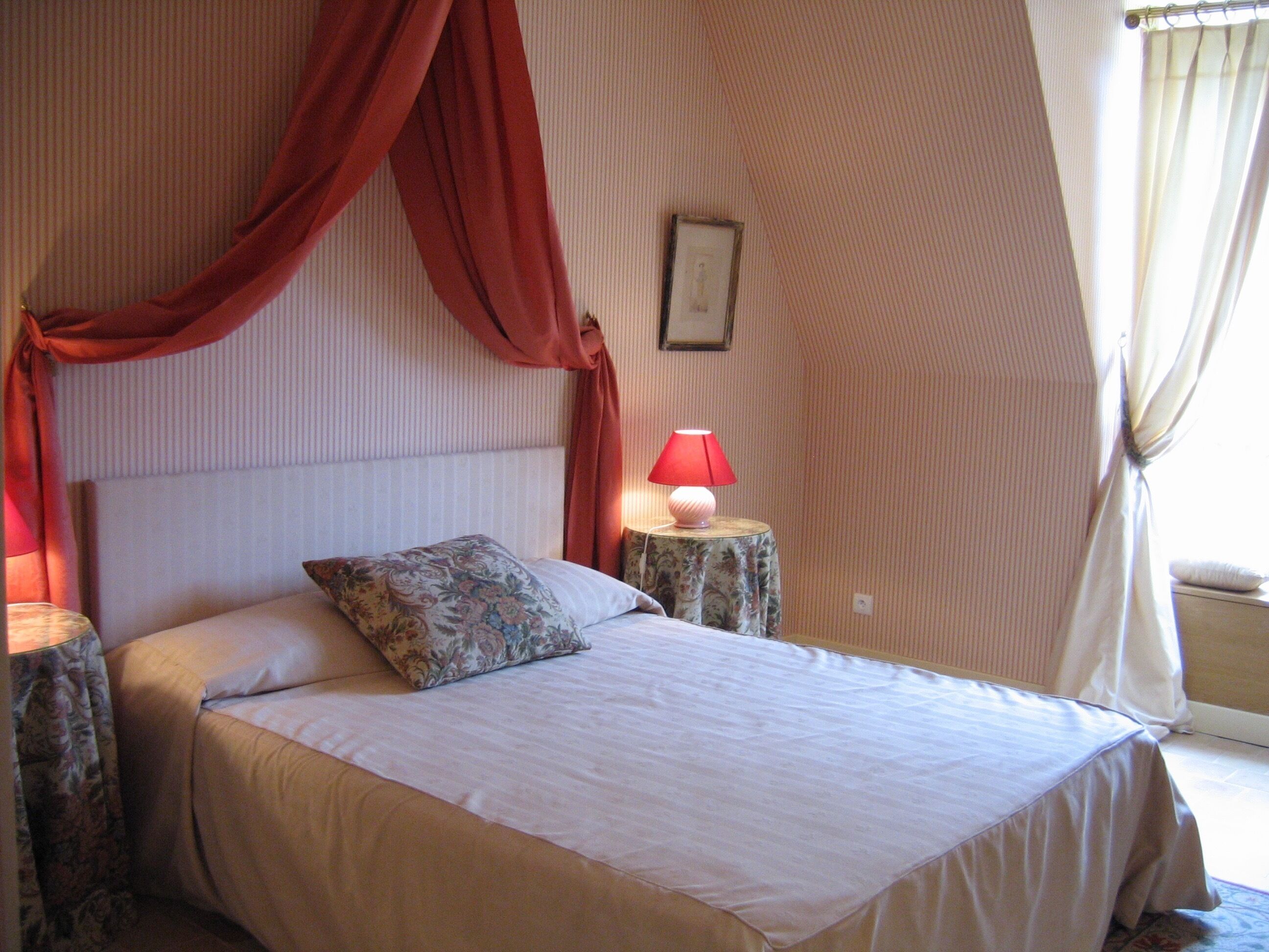 Une chambre à coucher avec un lit, une table de chevet, une lampe et une fenêtre avec des rideaux.
