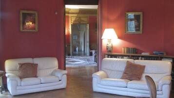 A room with two white sofas, a wooden floor with a geometric pattern, and a red wall with framed pictures.