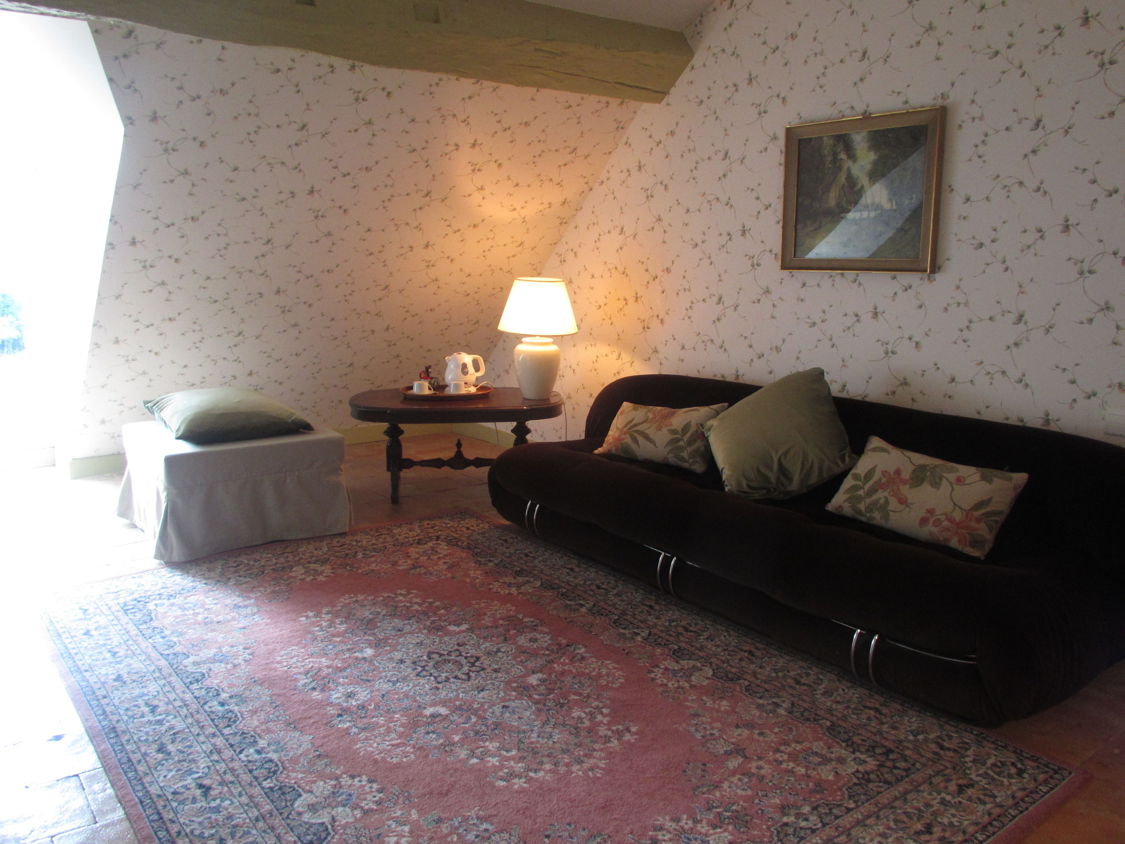Un salon chaleureux avec un canapé foncé, une petite table d’appoint, une lampe et un tapis à motifs floraux.