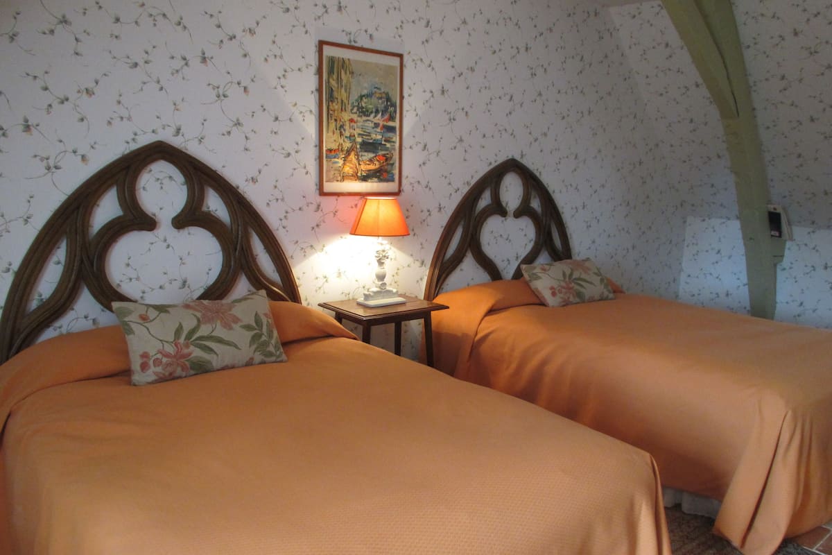 Una habitación con dos camas, una mesita de noche con lámpara, papel tapiz floral y un cuadro en la pared.