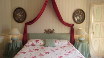 A bedroom with a four-poster bed, floral bedding, two bedside tables with lamps, and a door with a decorative panel.