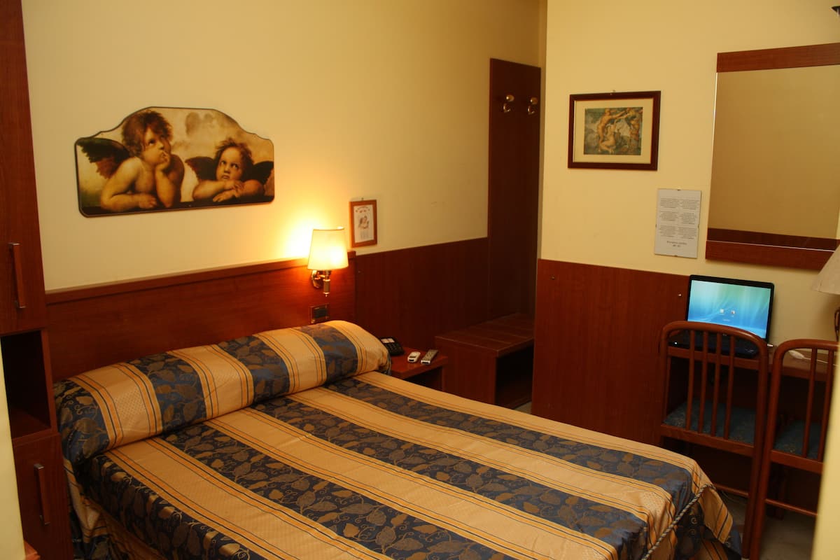 Una habitación de hotel con cama, escritorio, silla, lámpara y obras de arte en las paredes.