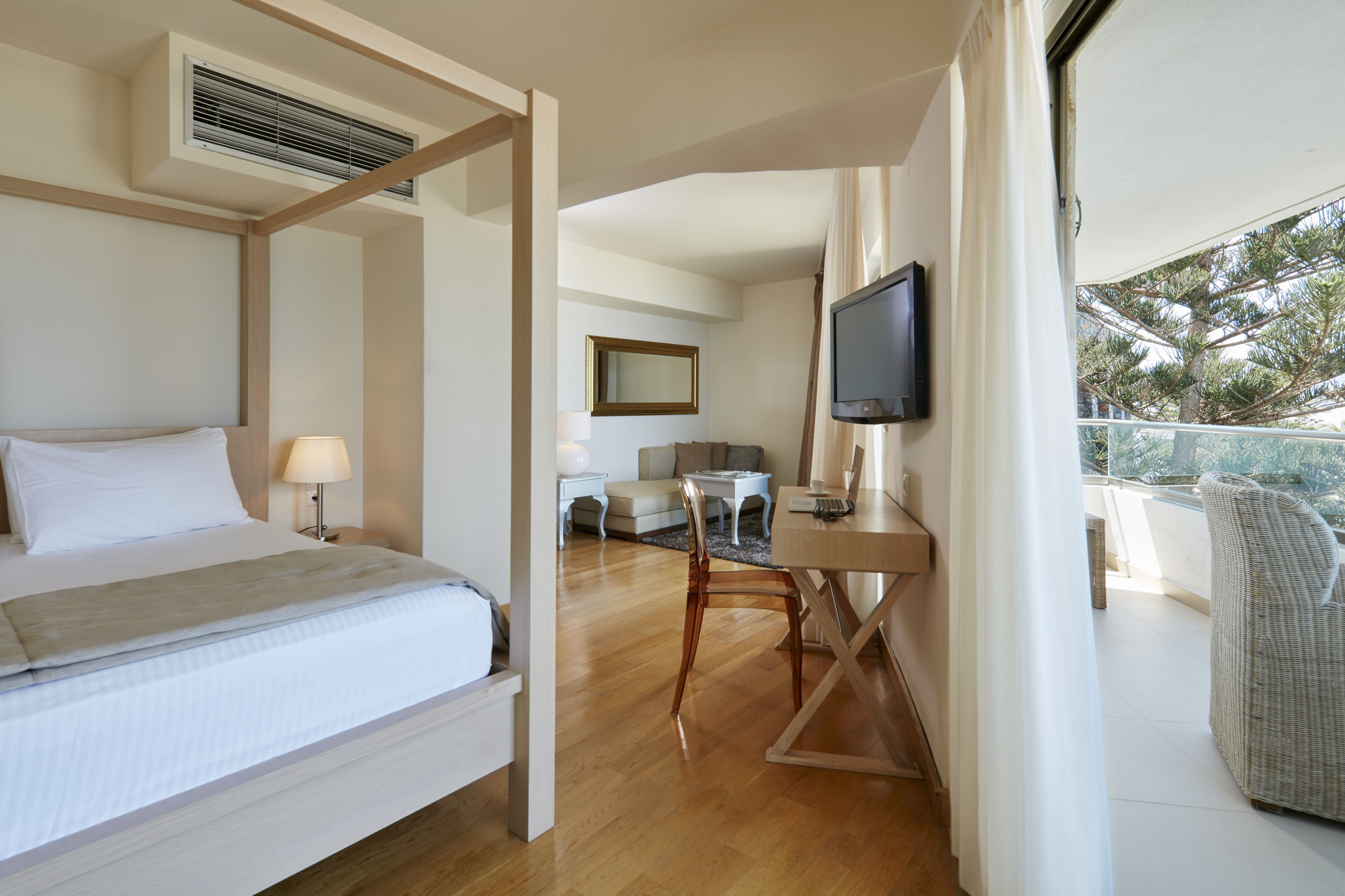 Ein Hotelzimmer mit Himmelbett, Schreibtisch mit Fernseher, Balkon mit Korbsessel und Essbereich mit Tisch und Stühlen.