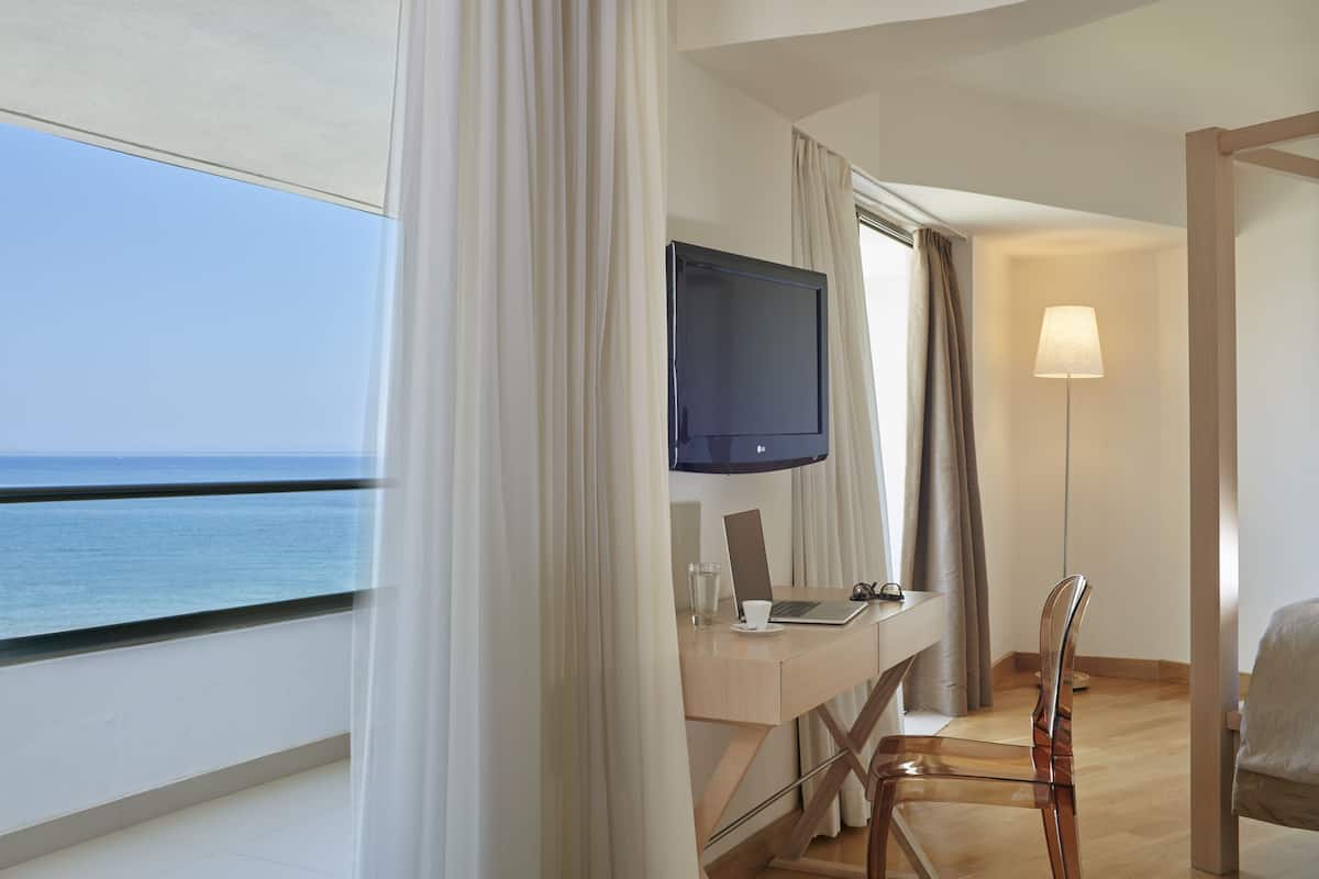 Habitación de hotel con balcón, un escritorio con una computadora portátil, televisión y una silla.