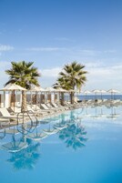 A pool area with lounge chairs and umbrellas, palm trees, and a clear view of the ocean.