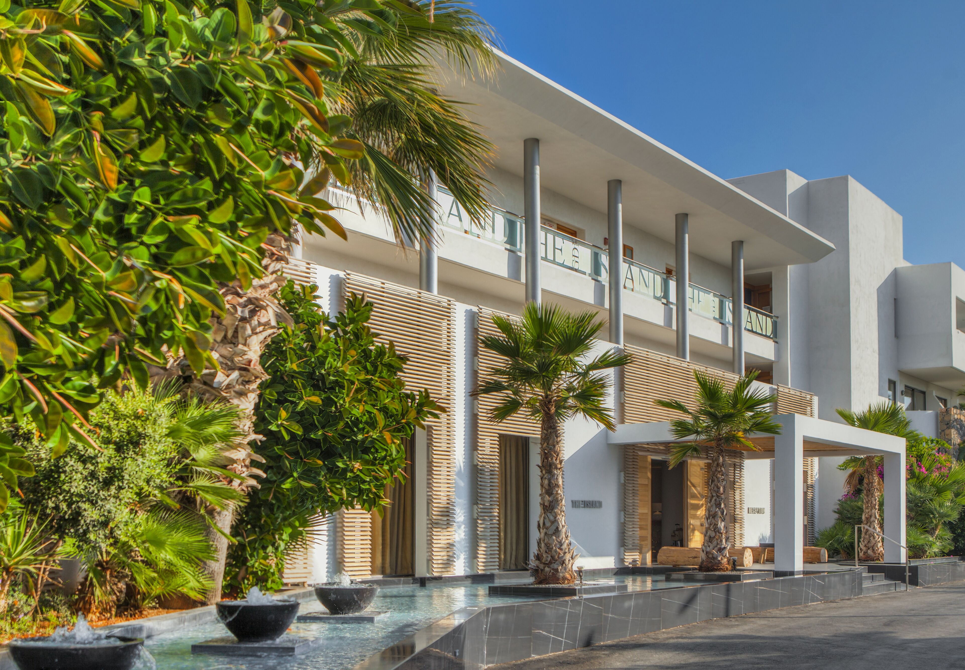 Un hotel moderno con piscina, palmeras y un cielo azul despejado.