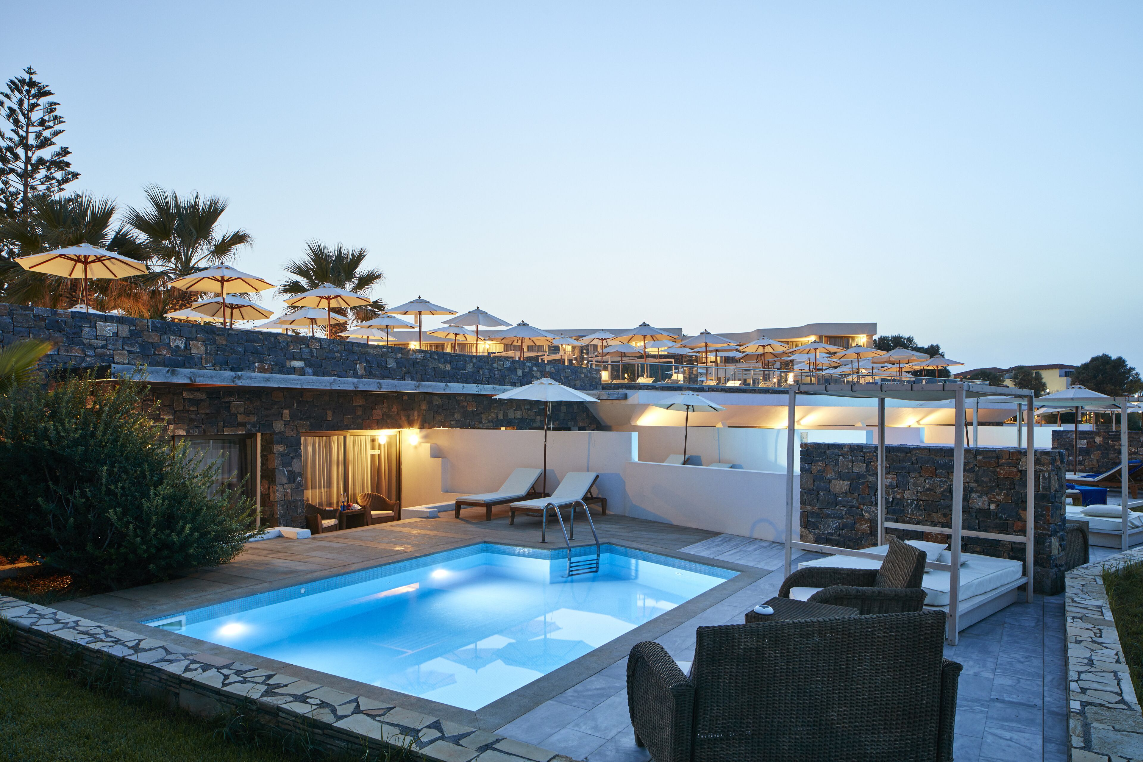 Une piscine entourée de chaises longues et de parasols, le tout bordé de murs et d’une terrasse en pierre.