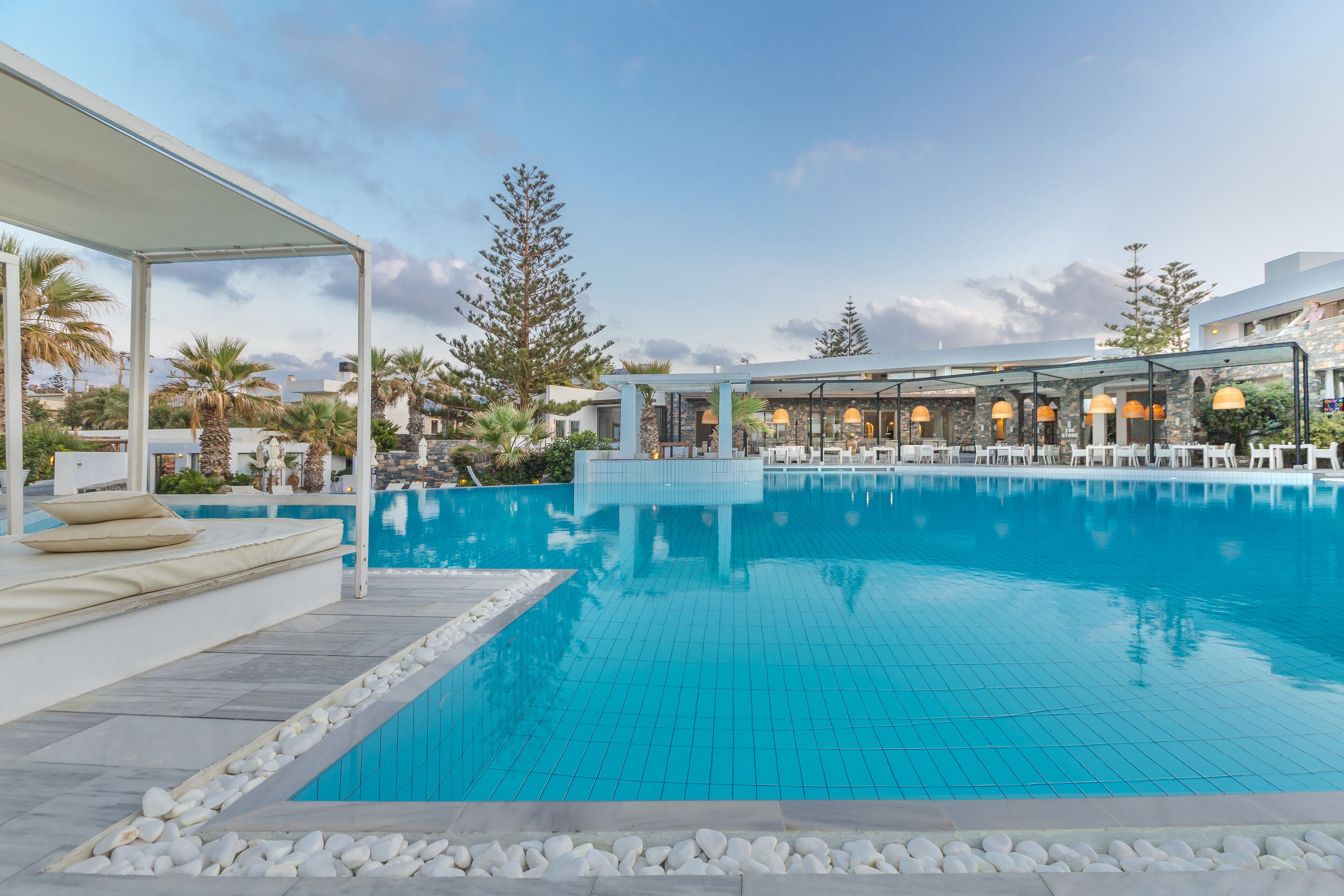 A swimming pool with a covered seating area and a restaurant in the background.